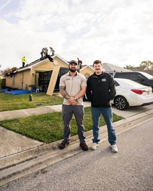 Braden and Blake Cox standing in front of a home while their crew tears off the old roof
